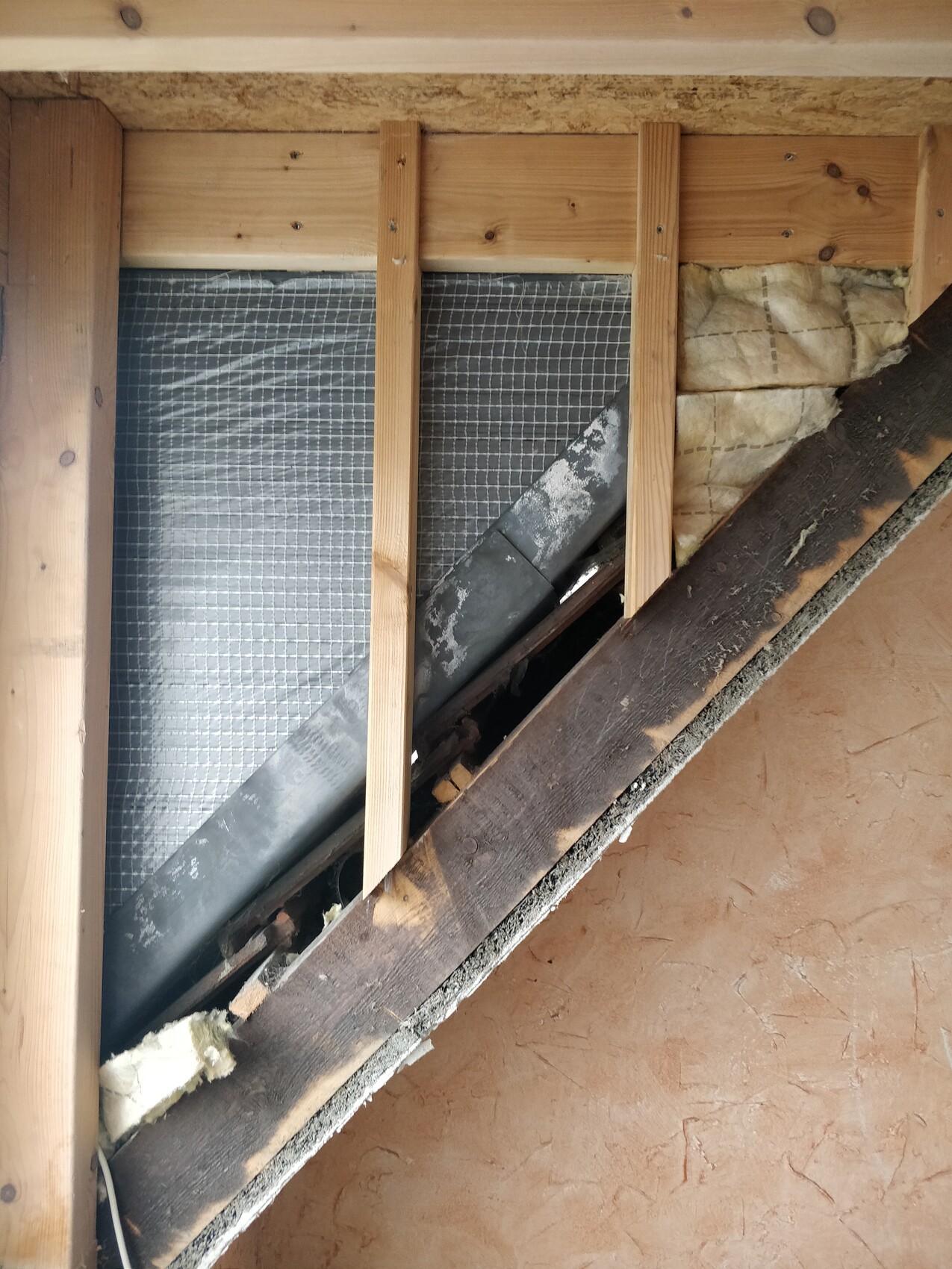 Attic with wooden studs, insulation, and a dark duct running along the wall.