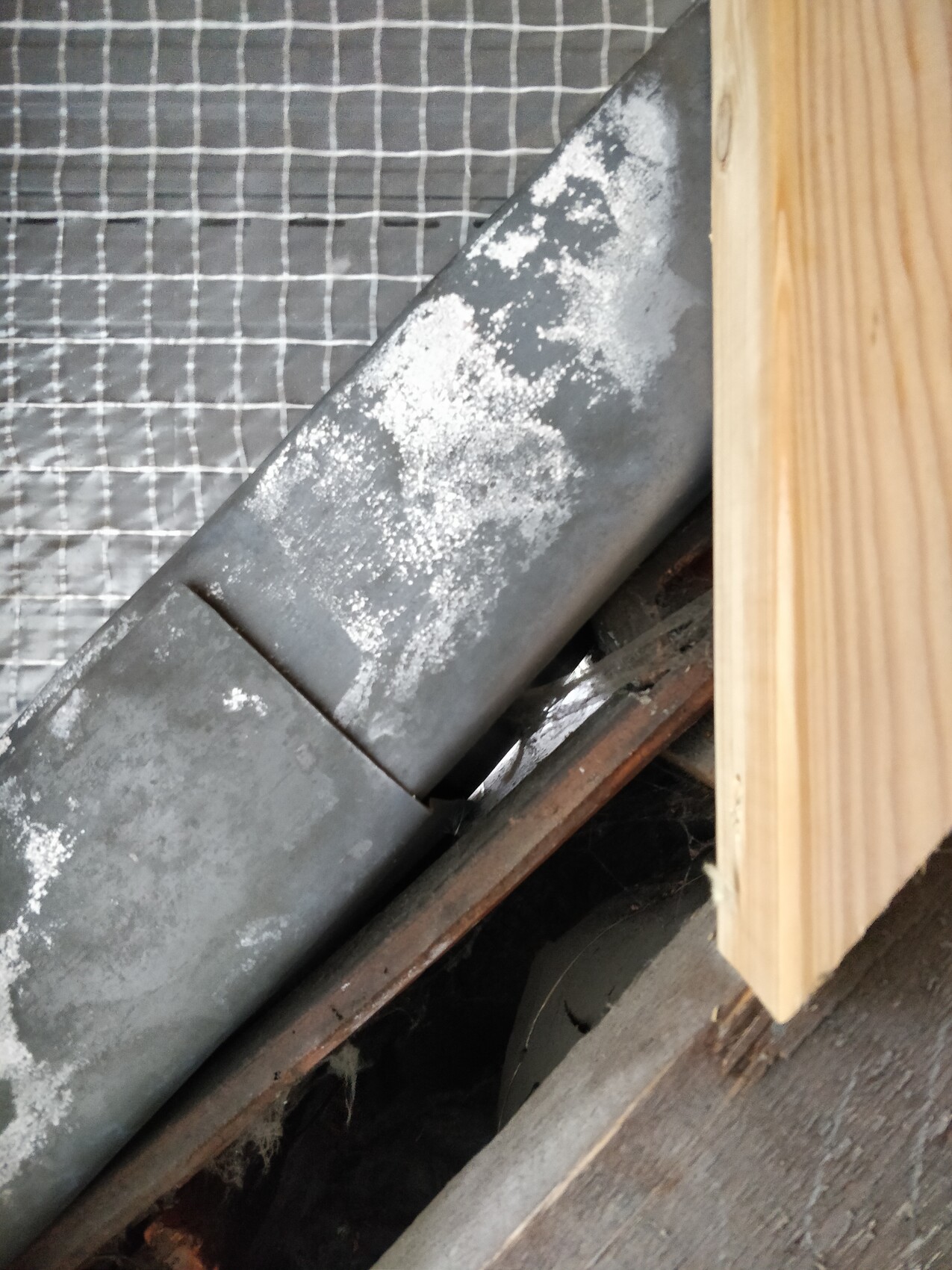 Close-up of a slanted metal pipe with lime deposits; wood and wire mesh beside it.