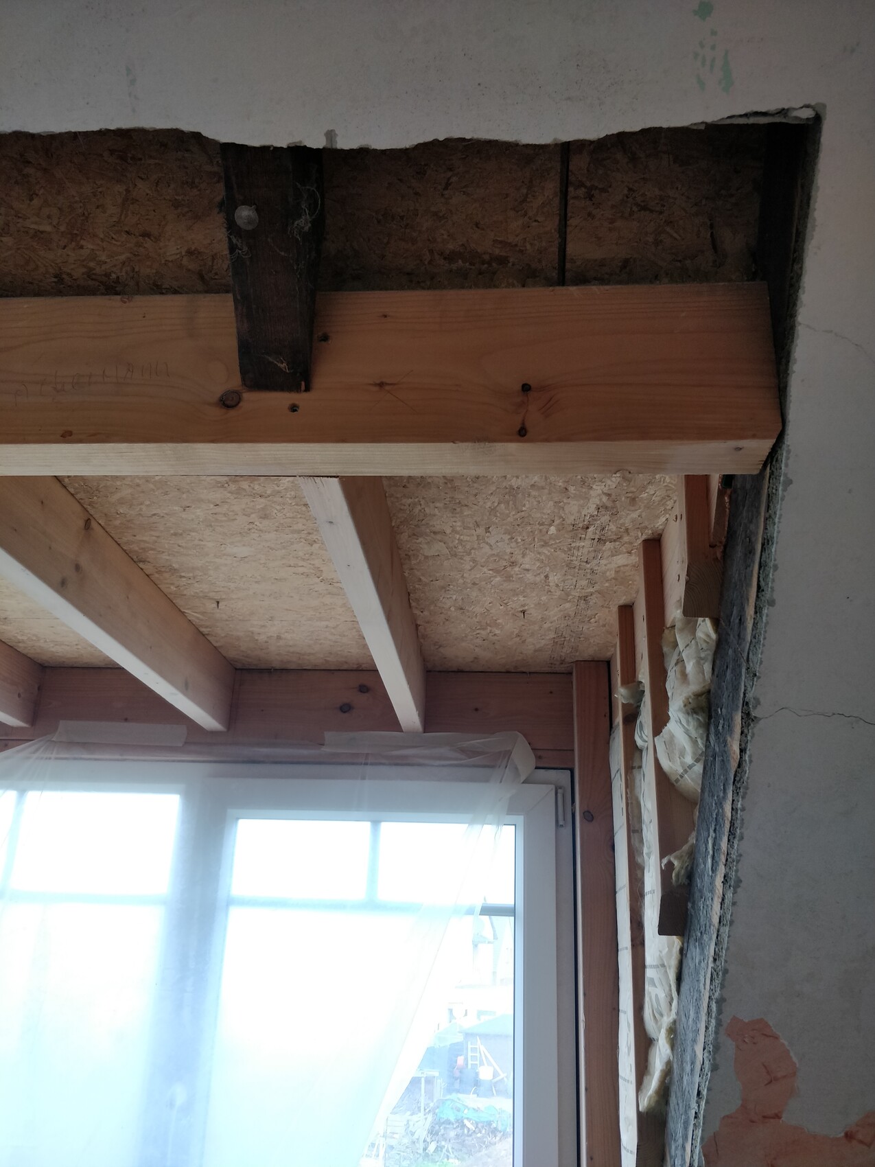 Interior of a construction site: exposed ceiling with wooden beams, window covered with membrane.