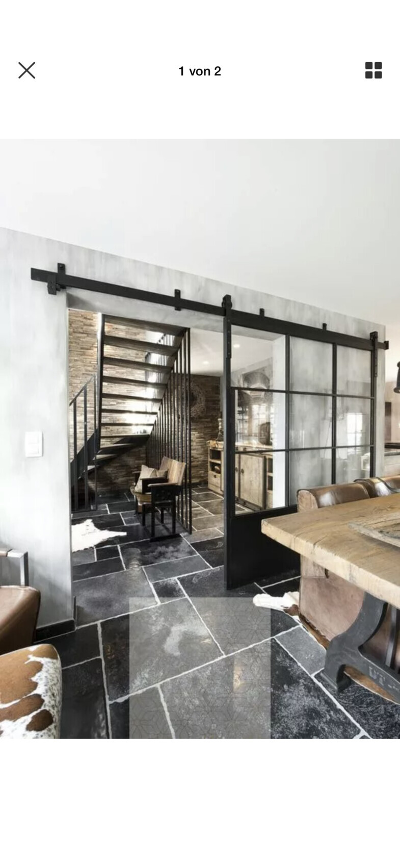 Offener Innenbereich mit schwarzer Stahltreppe, Glas-Schiebetüren, Steinboden und Holztisch