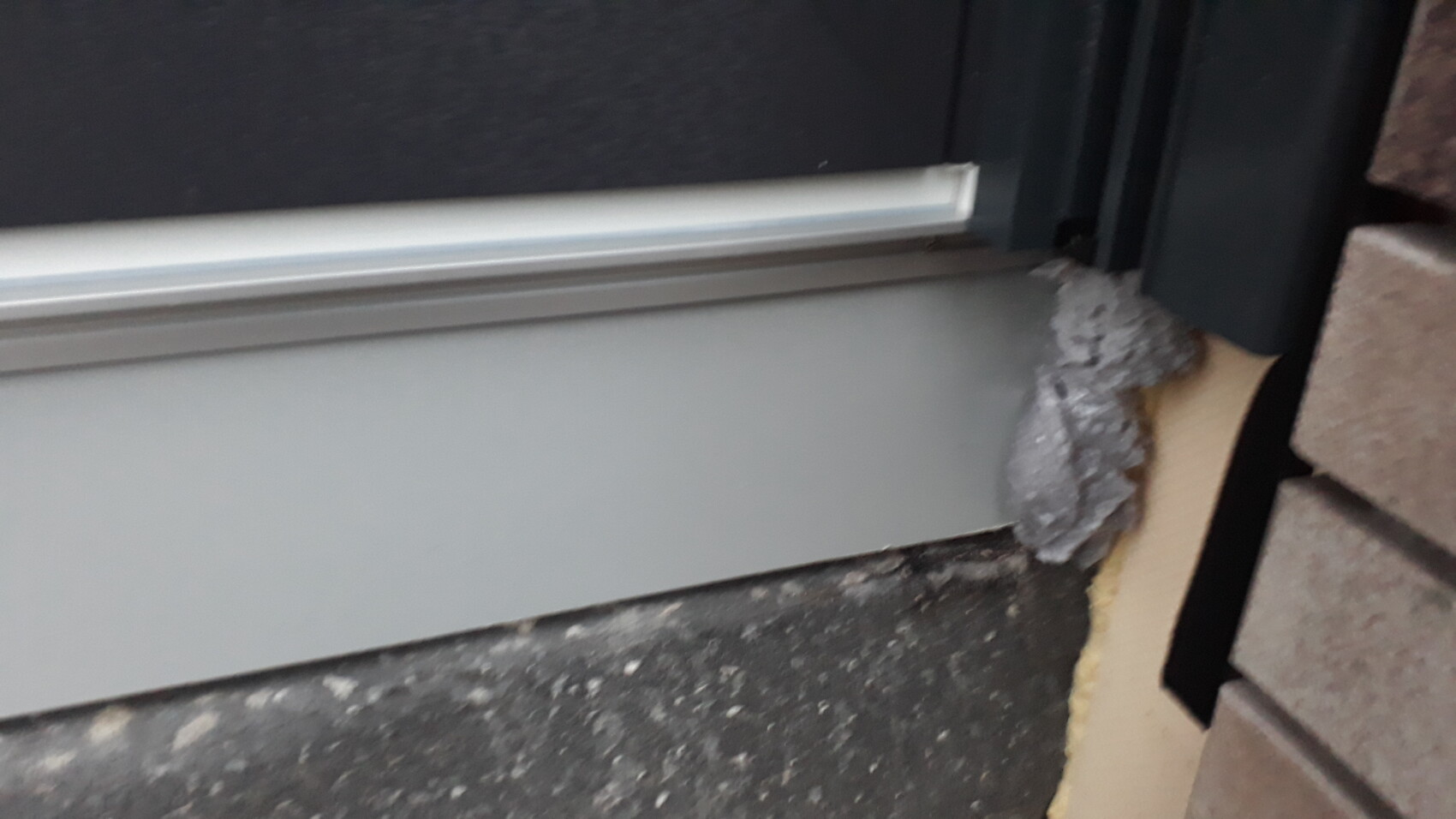Unterkante einer Tür mit Dichtungsleiste; grauer Schaumdichtung füllt den Spalt neben Steinboden.