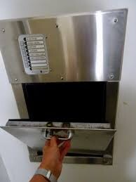 Wall-mounted metal box with a drop flap; a hand reaches in