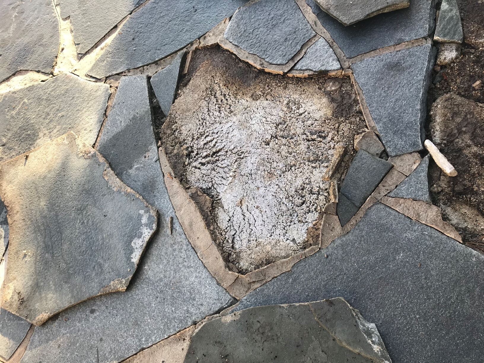 Unregelmäßiges Steinpflaster aus flachen Platten mit zentraler, staubiger Vertiefung und Rissen.