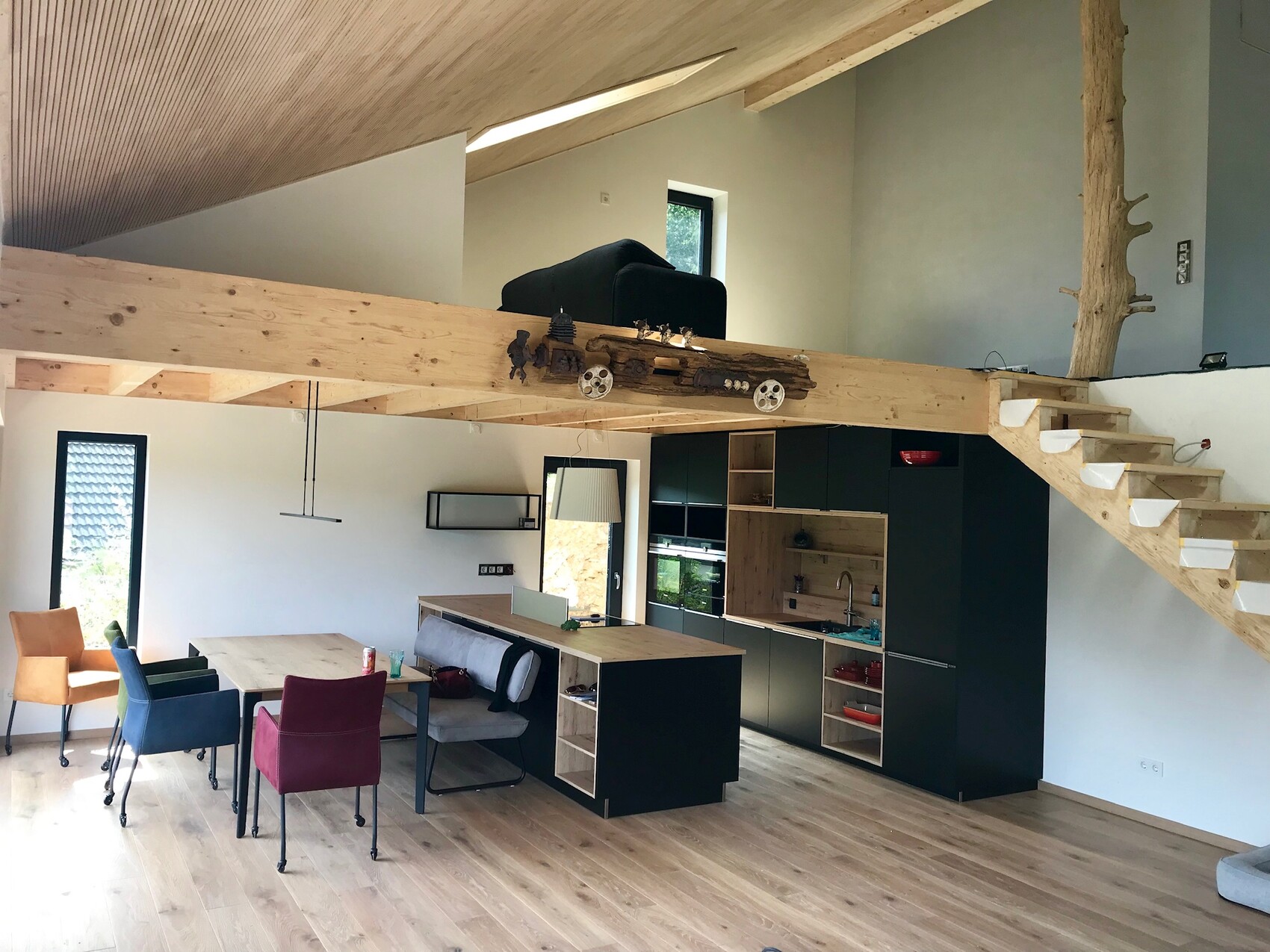 Open interior with kitchen, dining table, colorful chairs, and wooden loft gallery.