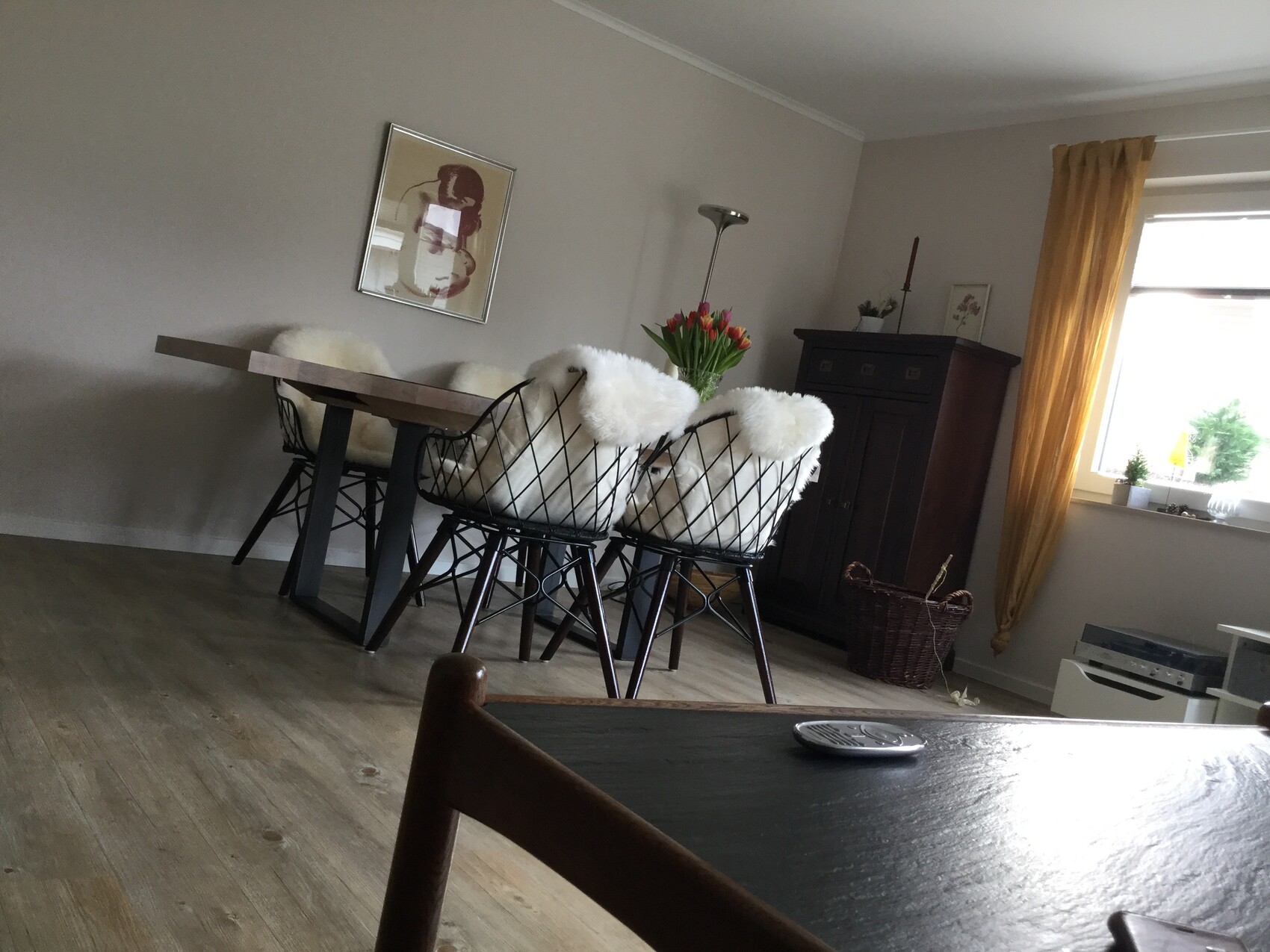 Living room with dining table, chairs with white fur covers, tulips, dark cabinet, golden curtains.