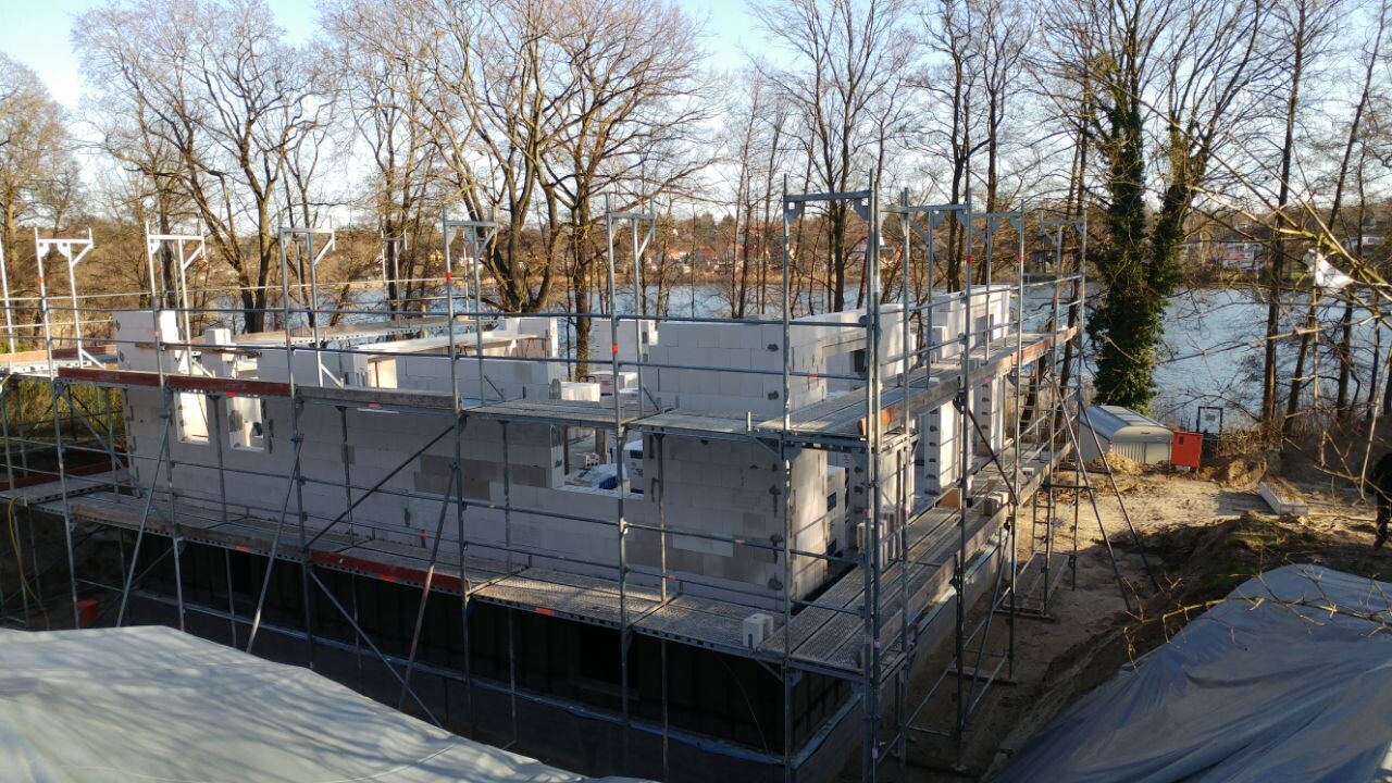 Shell construction made of concrete blocks on scaffolding at the riverbank, surrounded by bare trees in winter.
