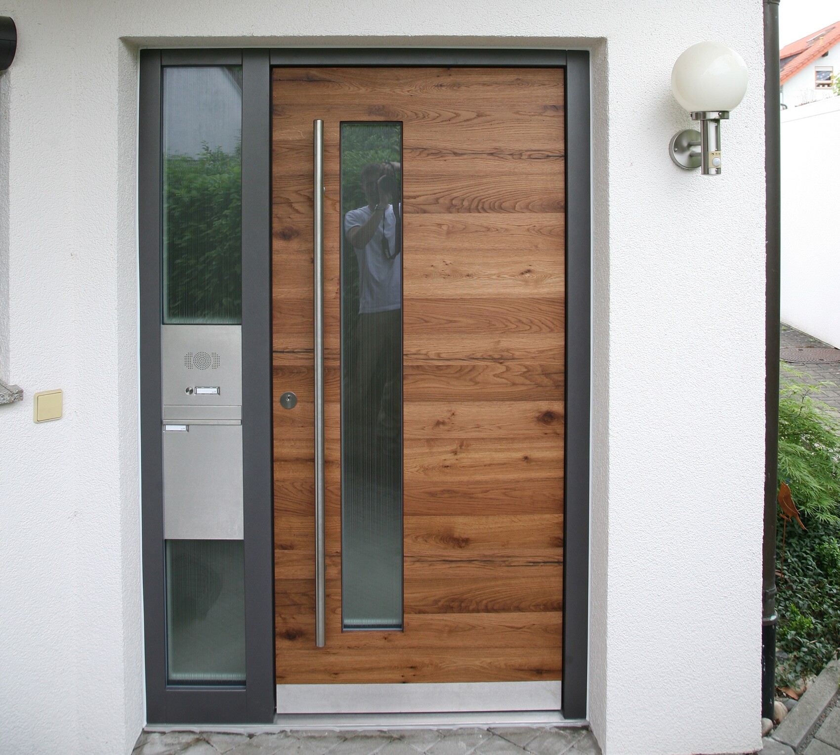 Modern wooden door with long metal handle, vertical glass window, and glass sidelight.