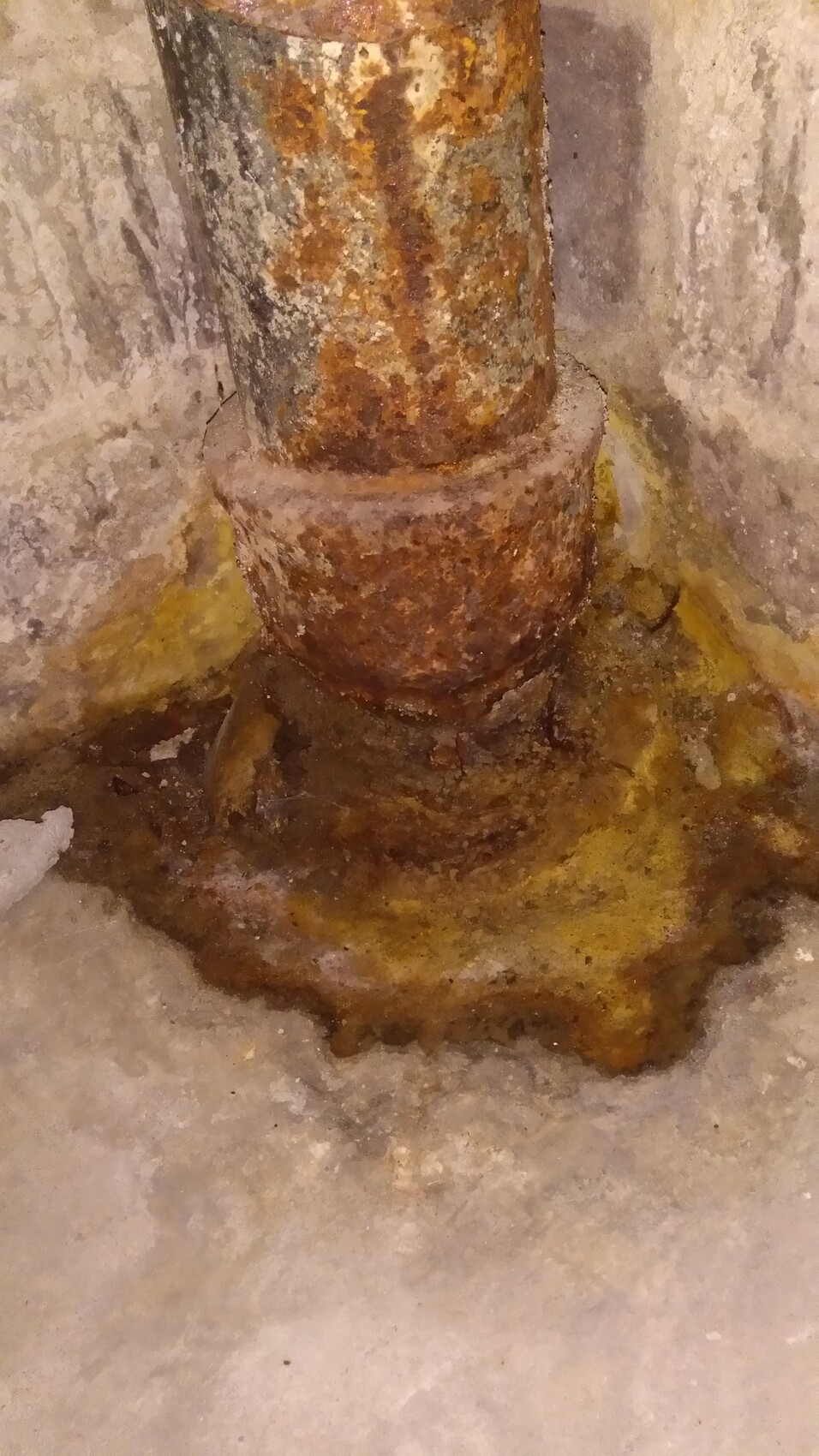 Rusted pipe in basement floor with moisture and water damage.