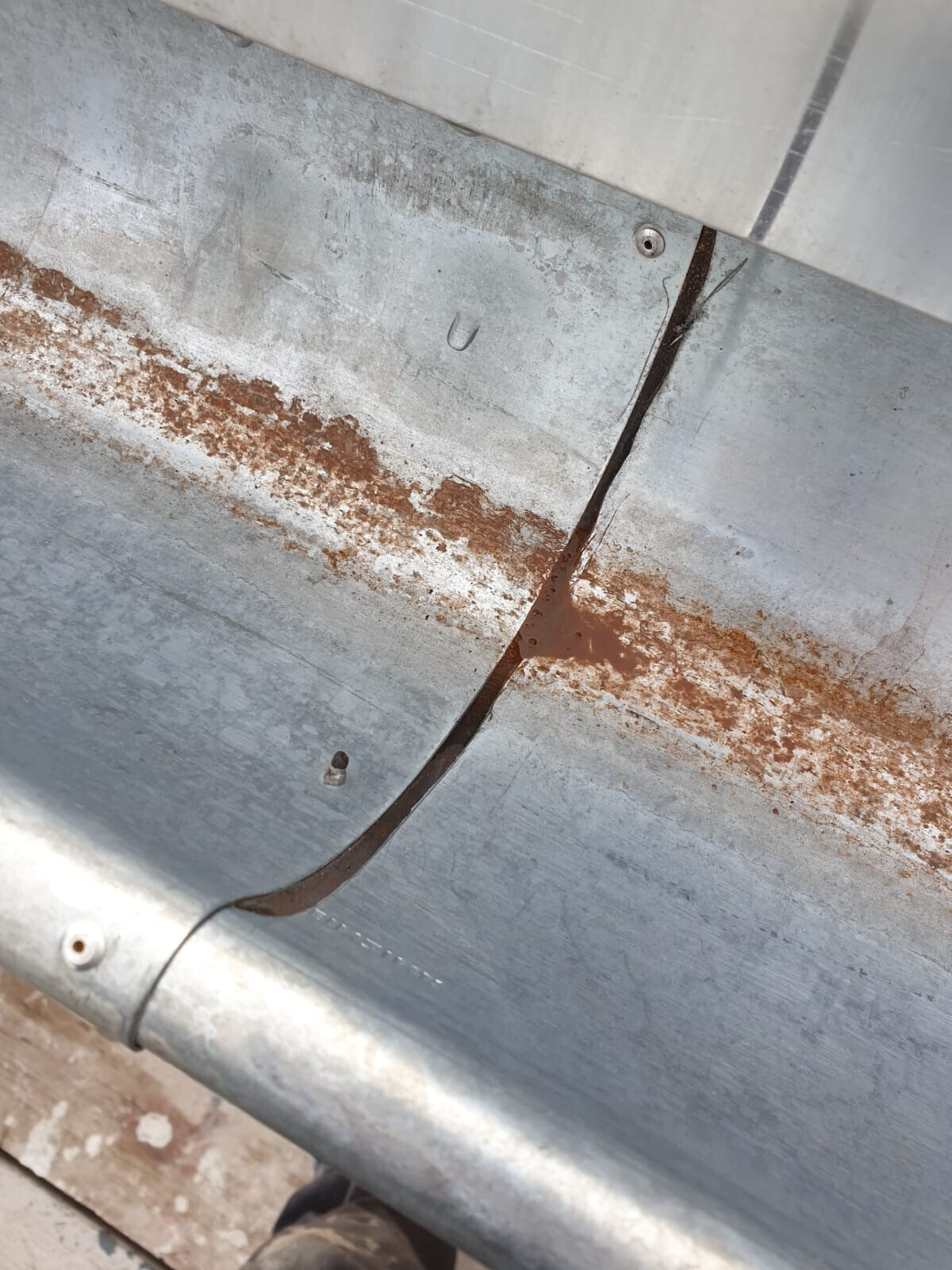 Close-up of a metal sheet with rust stains along a seam and screw heads.