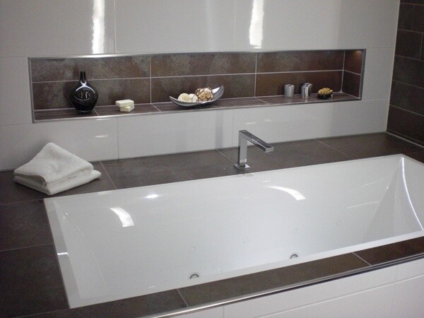 Modern bathroom with integrated bathtub, faucet, and shelf with decorative objects.