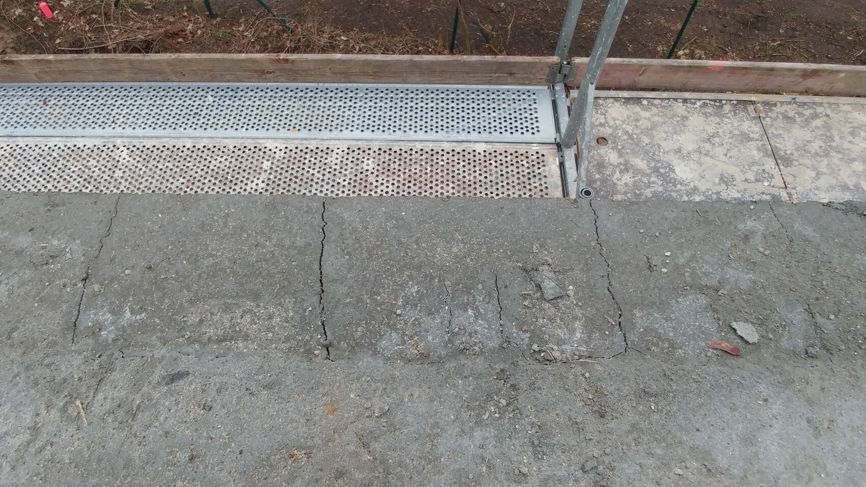 Concrete floor with cracks; next to it perforated metal grid and railing post of a construction.
