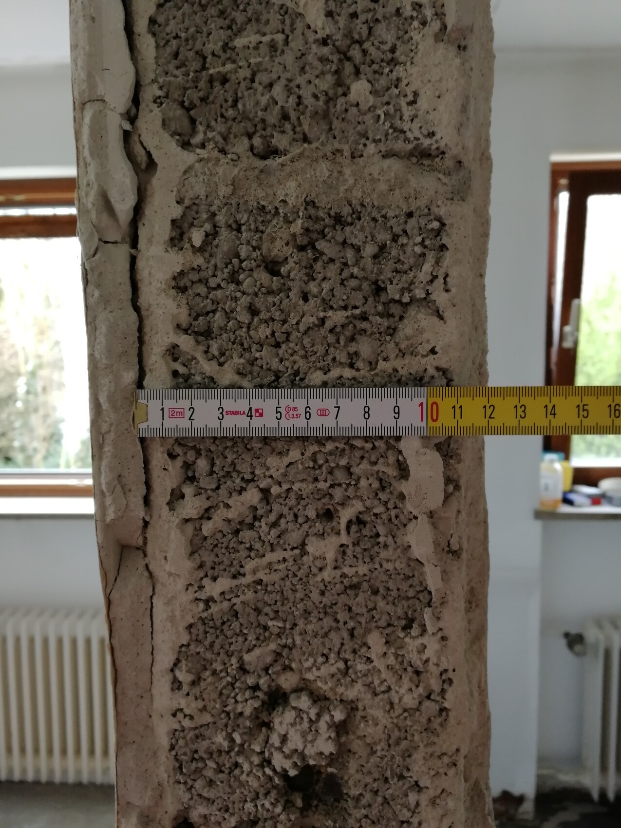 Porous concrete pillar with rough surface texture; measuring tape runs across the middle.
