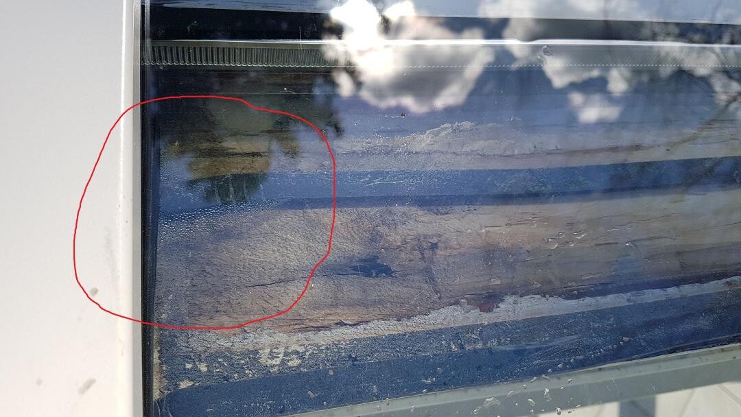 Fensterscheibe mit Staubflecken und Schlieren, weißer Rahmen links.