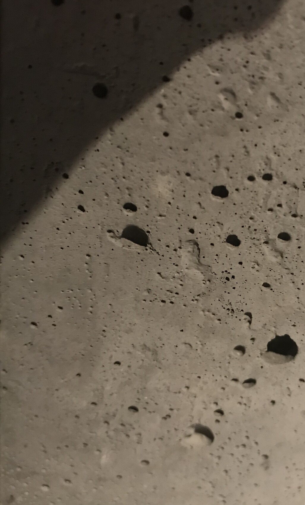 Porous stone or concrete surface with many round holes and diagonal shadow.