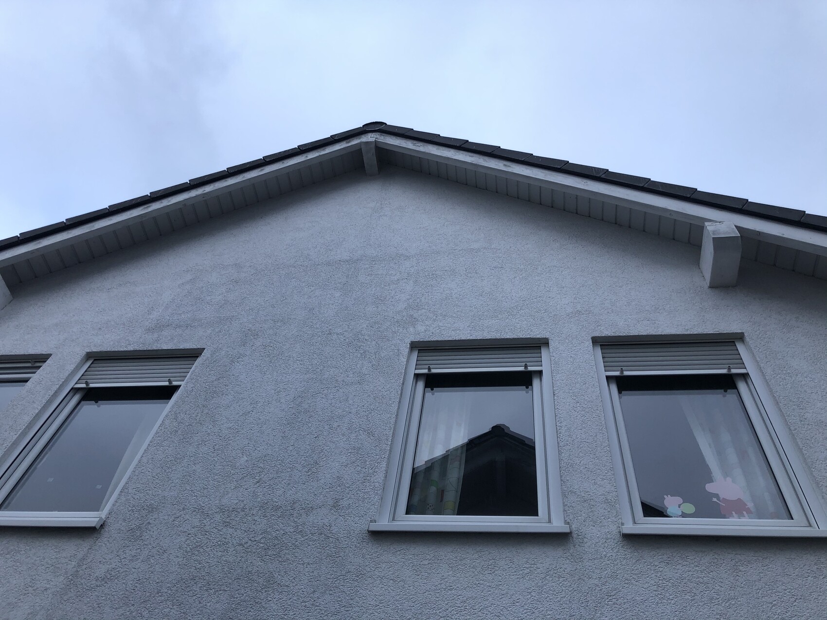 Exterior view of a gray house from below; three windows under the roof, blue sky