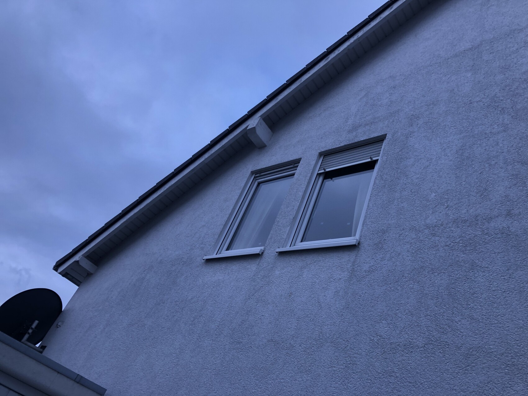 Exterior facade of a house with two windows under the roof, bluish tinted sky.