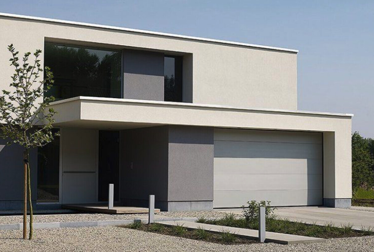 Modern white villa with flat roof, large garage, driveway, and gravel garden.