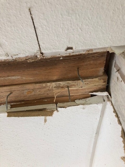 View of a damaged ceiling/wall: exposed wooden beam, nails, and crumbling plaster.