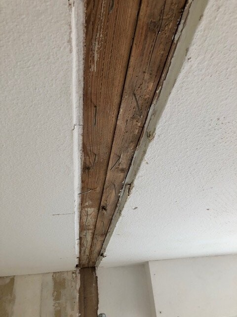 Exposed wooden beam in a plastered ceiling with cracks