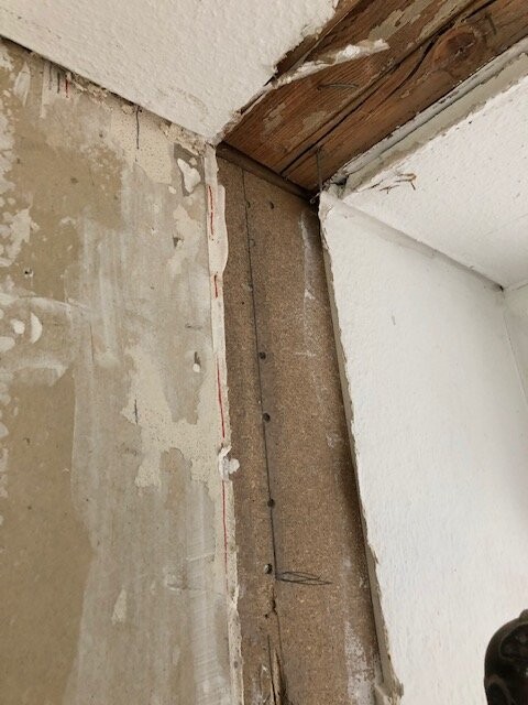 Renovation area: corner with visible wooden beam on the ceiling, unplastered wall, and nails.