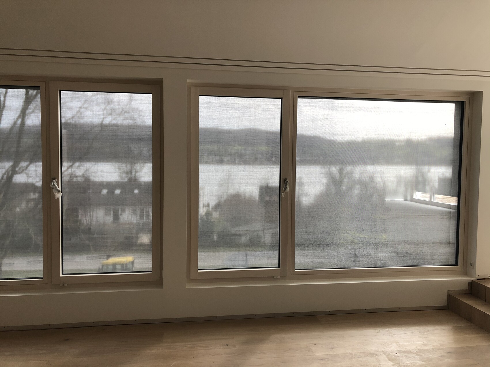 Large living room window with lake and mountain view, interior with wooden floor.