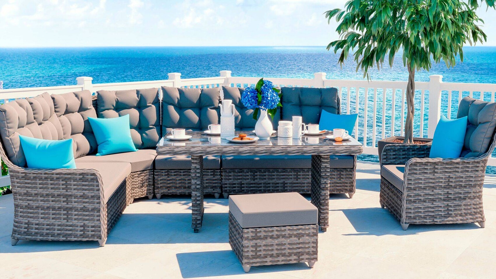 Terrace seating by the sea: gray rattan sofa set, blue cushions, glass table with hydrangea flower