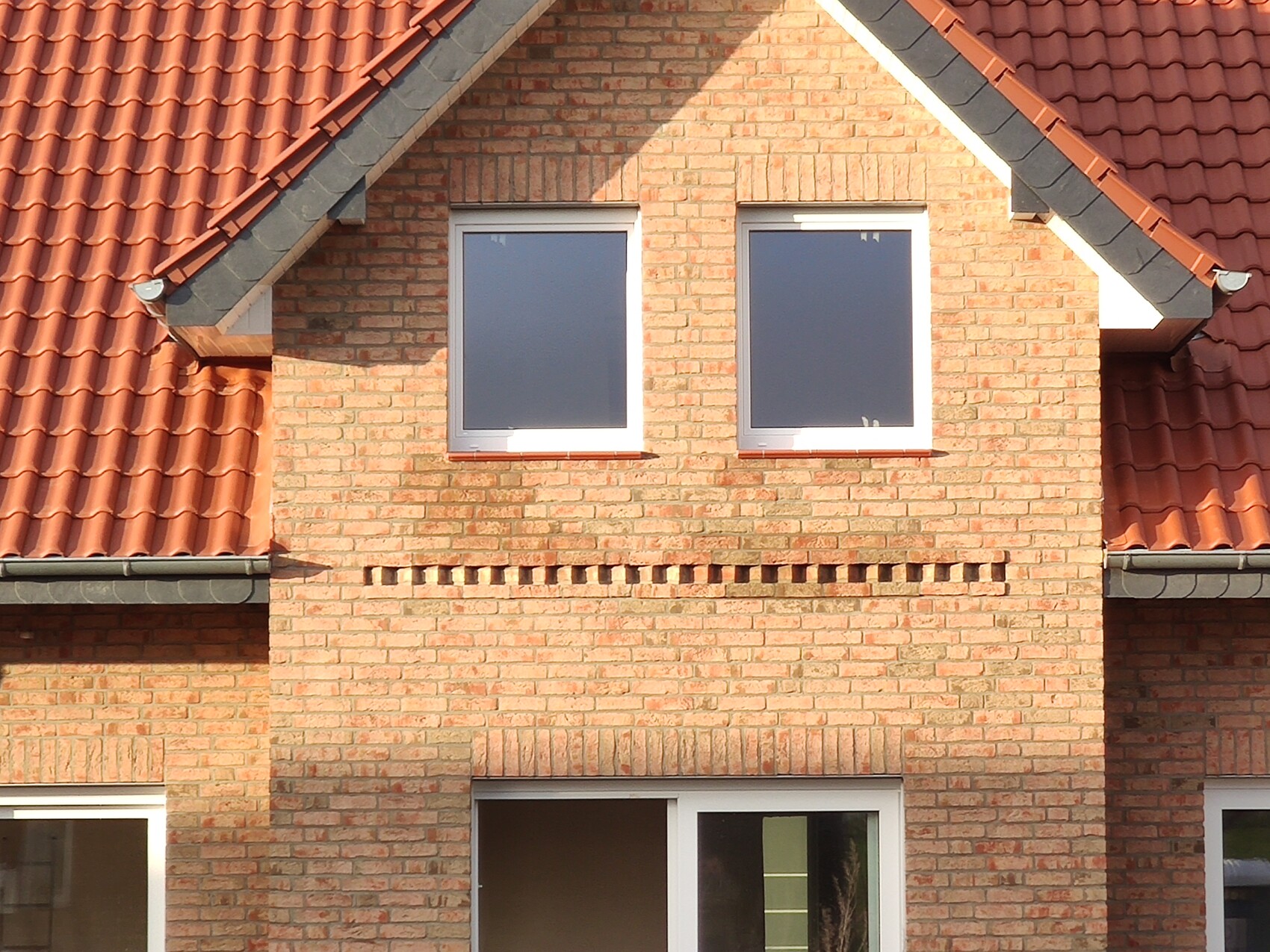 Vorderansicht eines roten Backstein-Hauses mit schrägem Dach und zwei Fenstern