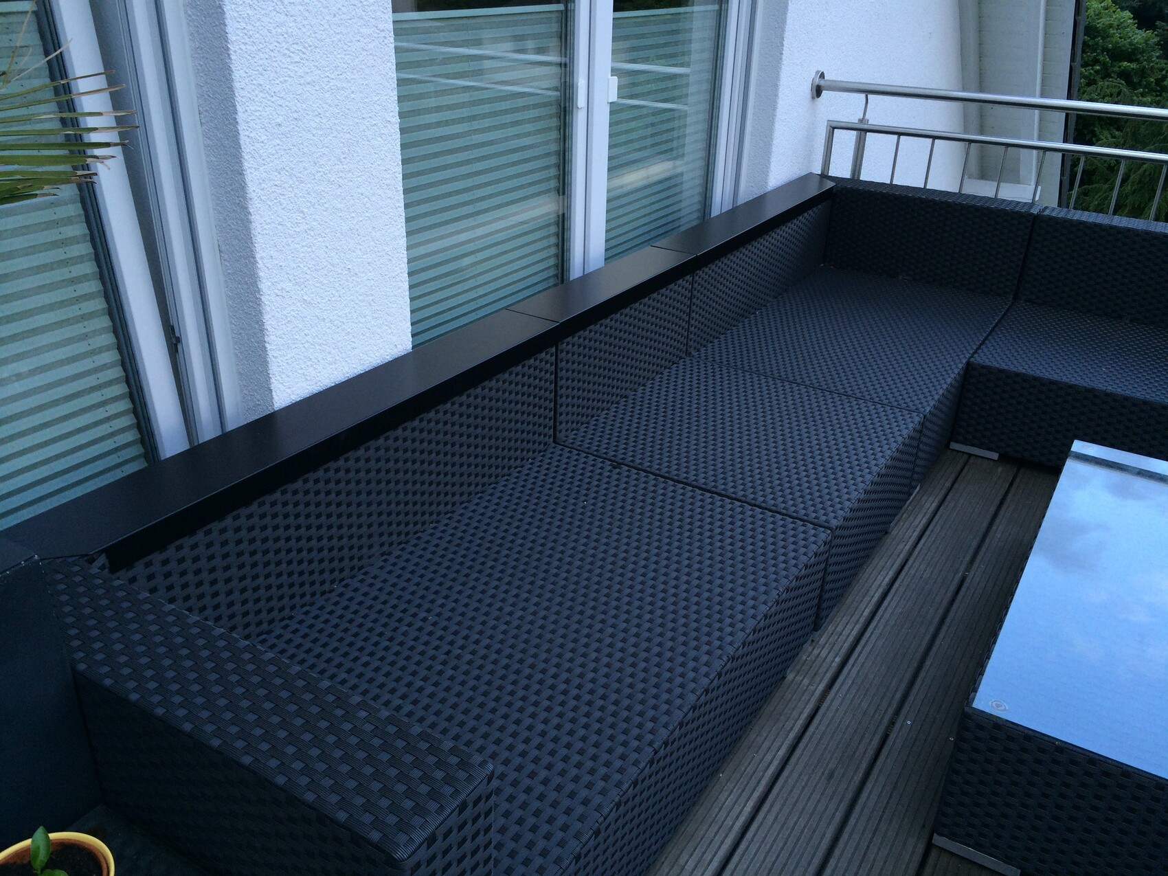 Gray-black outdoor seating set on balcony with glass table and wooden deck.