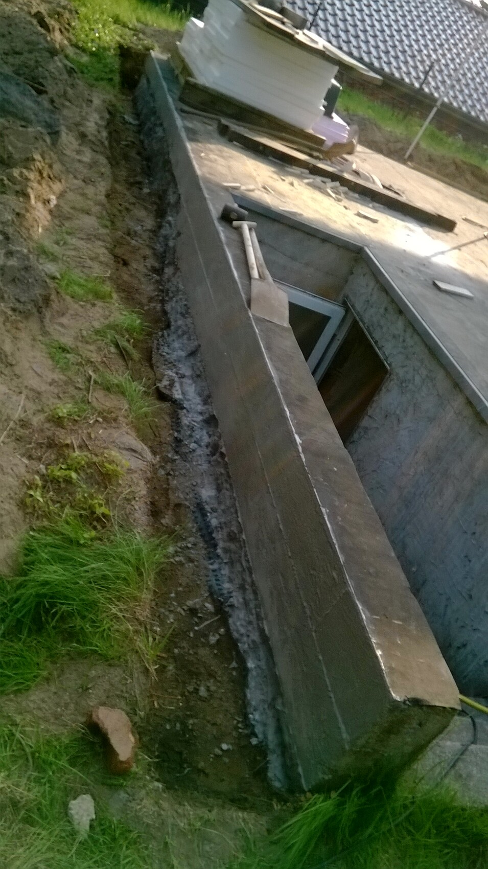 Excavation with concrete walls, open basement door opening, shovel leaning on wall, construction boards on top.