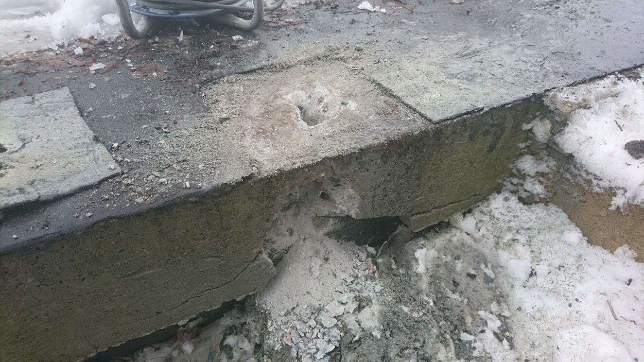 Beschädigte Betonstufe mit Loch, losem Geröll und Schnee rundherum