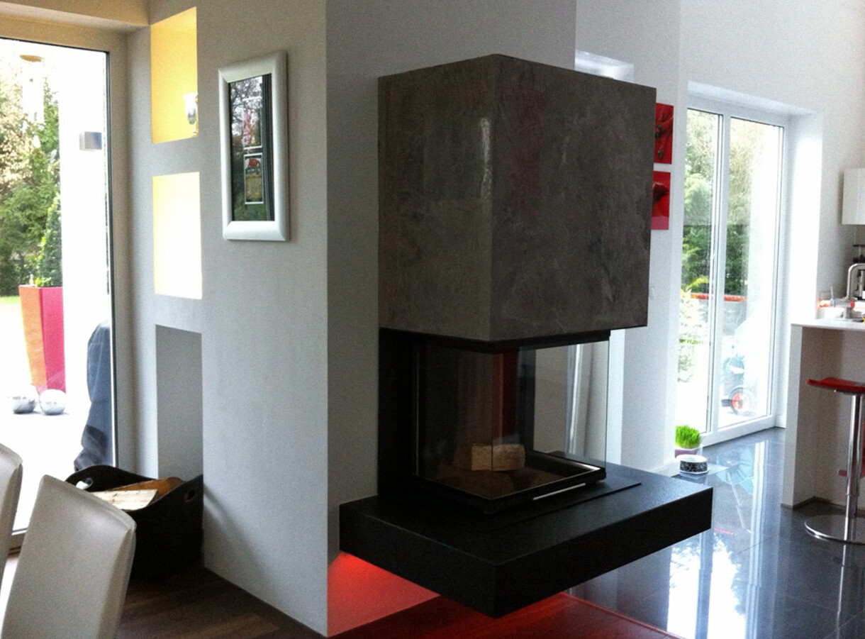 Modern living room with central fireplace, open kitchen and glass doors to the garden.
