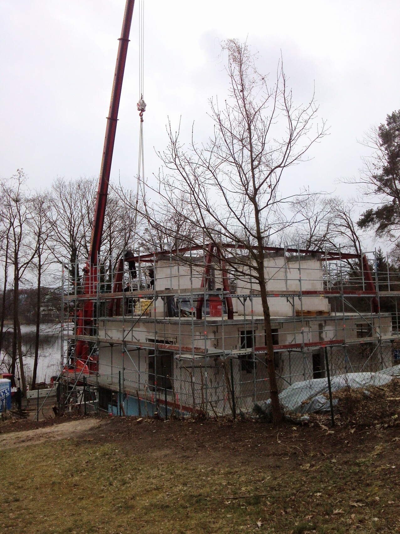 Construction site with scaffolding, unfinished building, crane on the left, bare trees in the foreground.