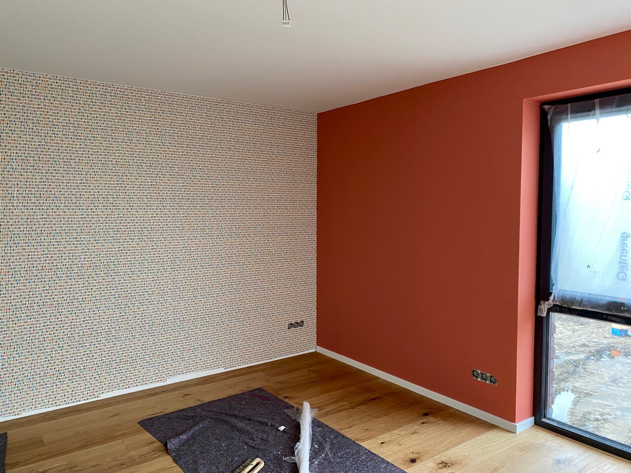 Renovation room: left mosaic wall, right red accent wall, window with protective film, wooden floor.