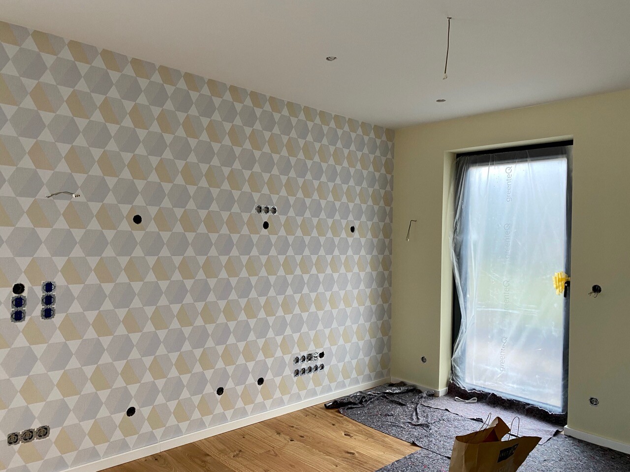 Renovated room with triangular accent wall, exposed outlets, and door with film.
