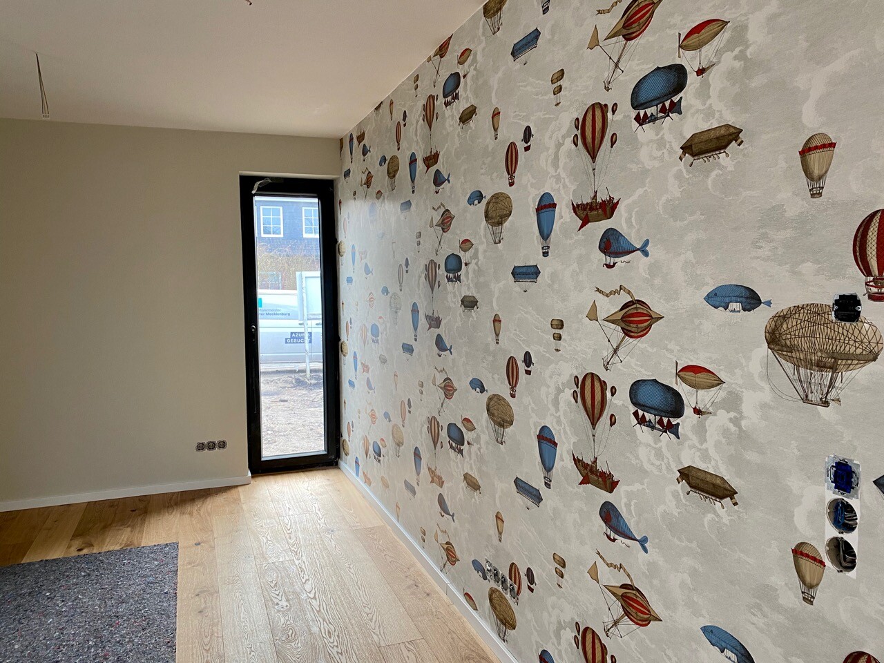 Bright interior with wallpaper featuring colorful hot air balloons, glass door, wooden floor.