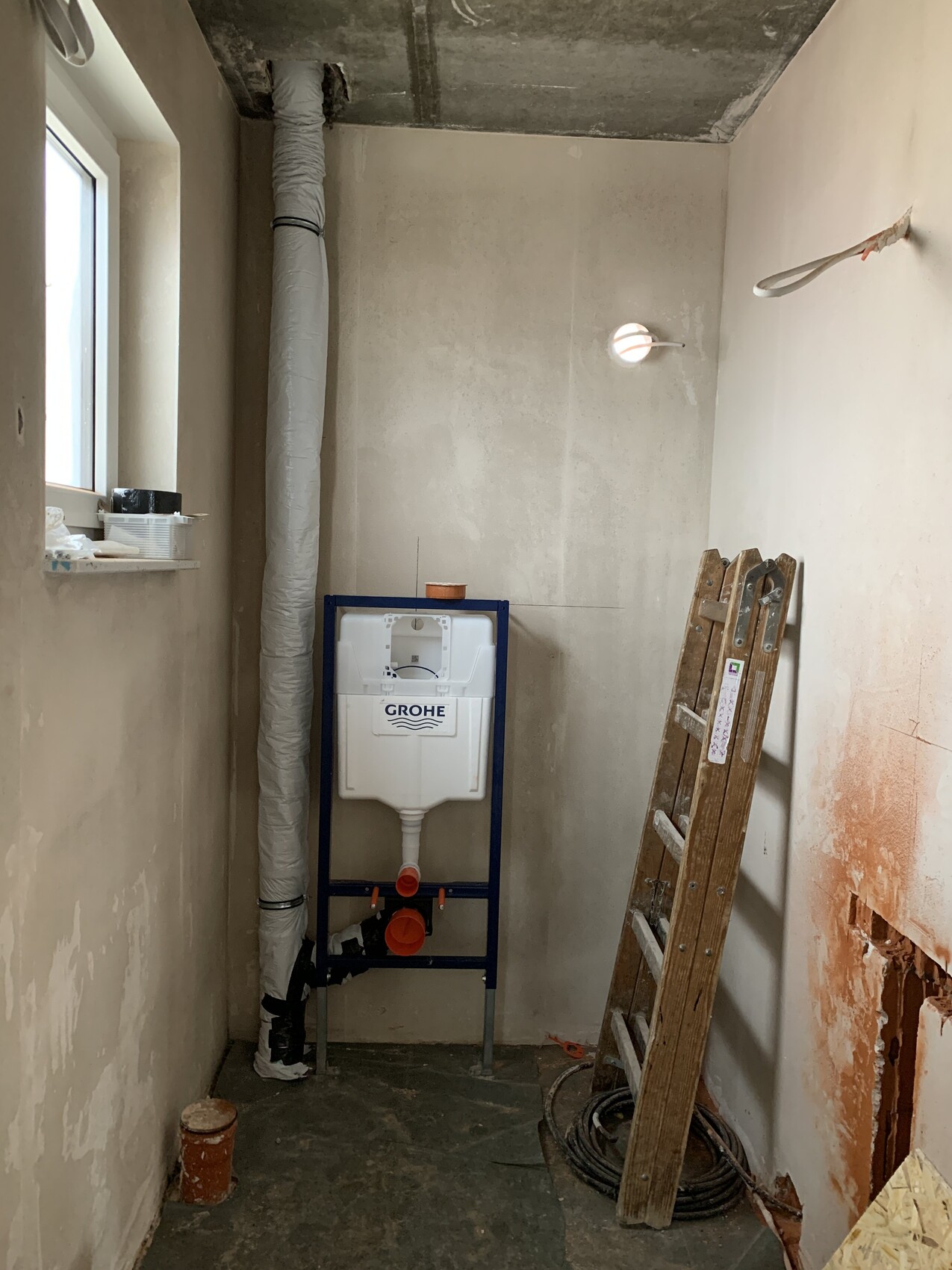 Bathroom construction site: Grohe flush tank on metal frame, insulated drain pipes, ladder, cables
