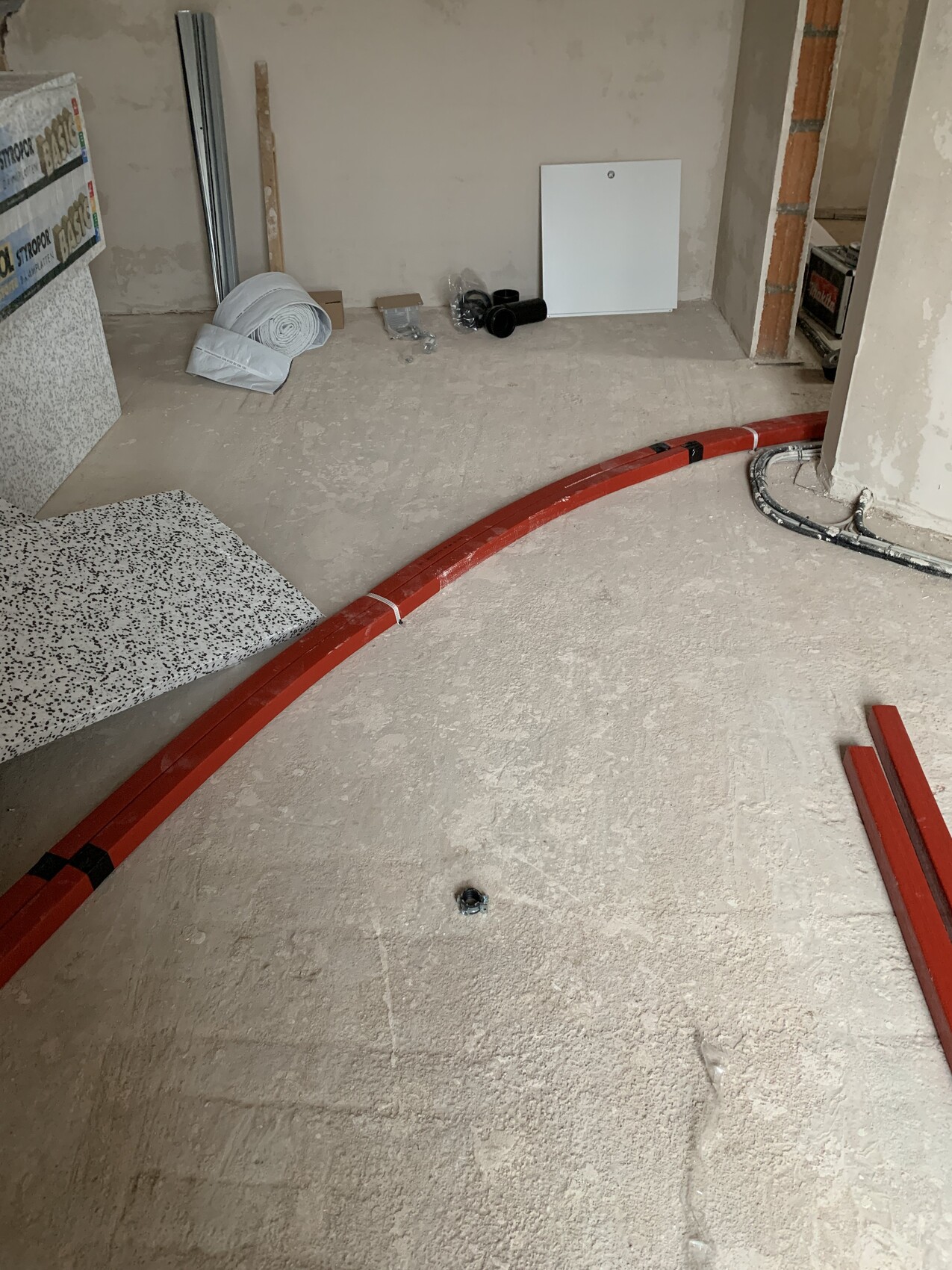 Red, curved pipe lying on unfinished floor; building materials and installations visible