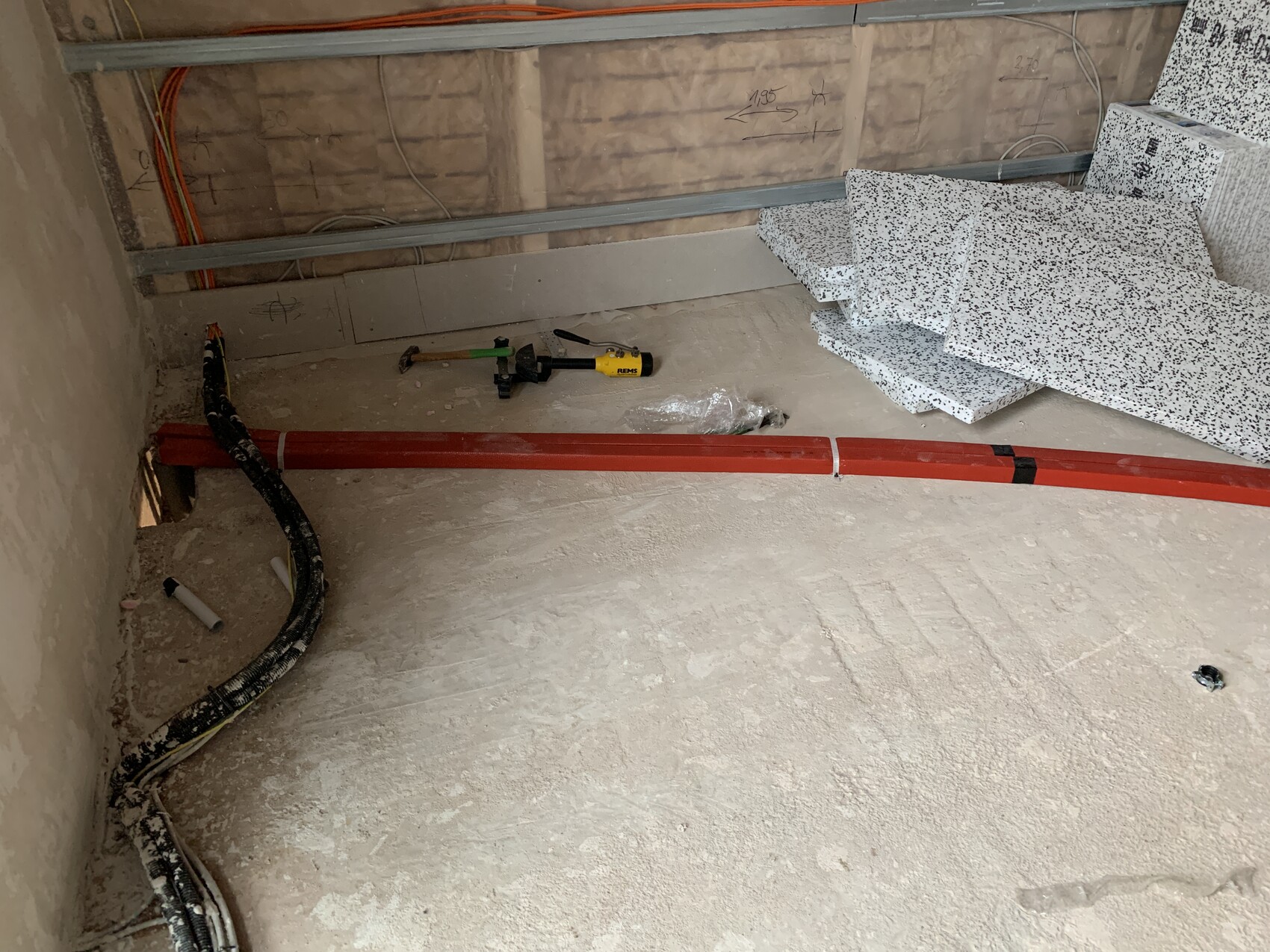 Construction site: red pipe over dusty floor, cables, tools, and stacked panels.