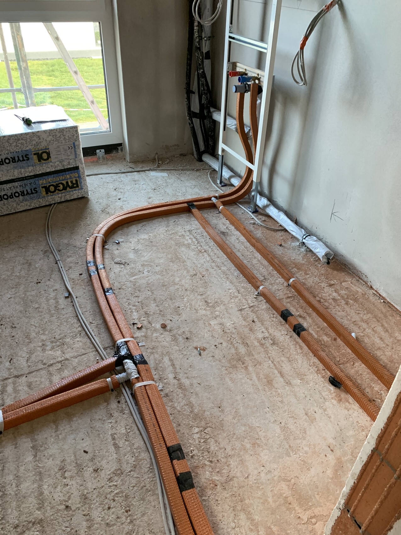 Interior construction site: orange PEX heating pipes run in the floor, cables lying beside.