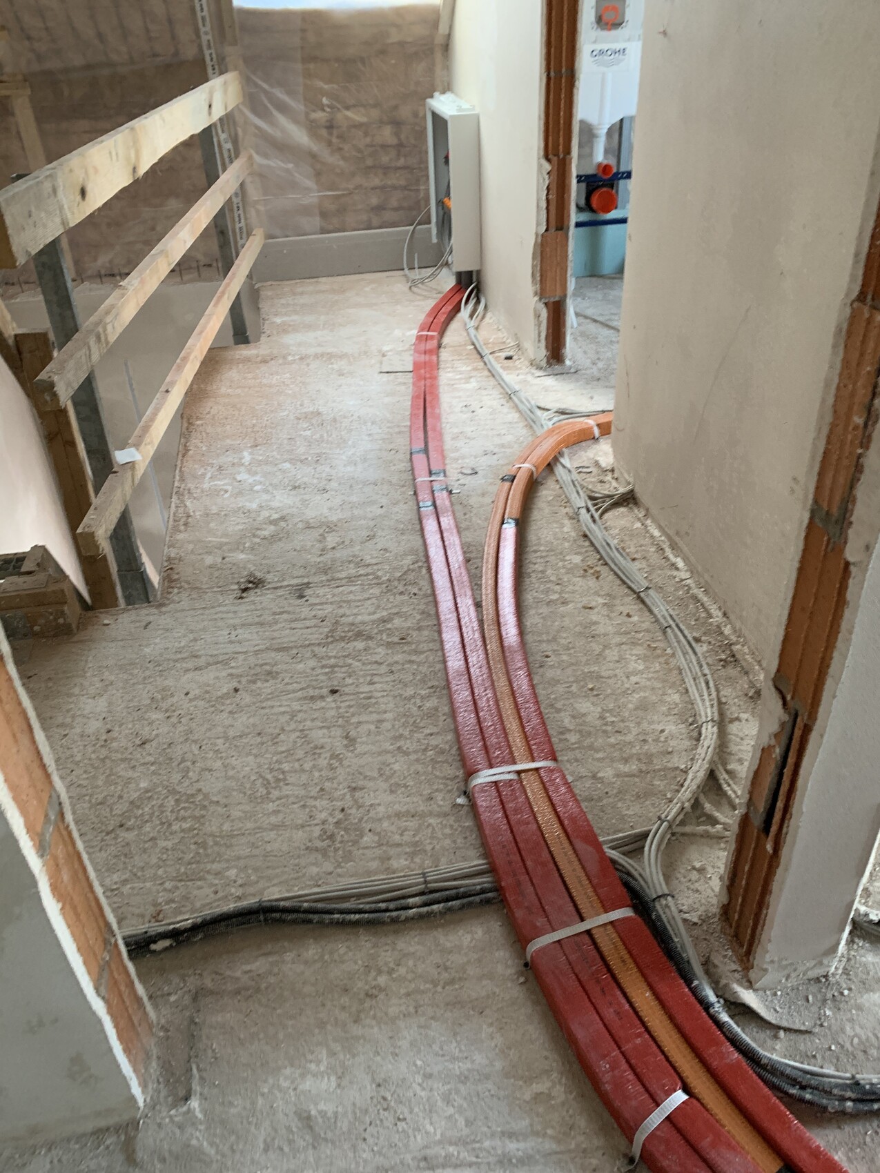 Construction hallway: several red heating pipes and cables lying loose on the floor.
