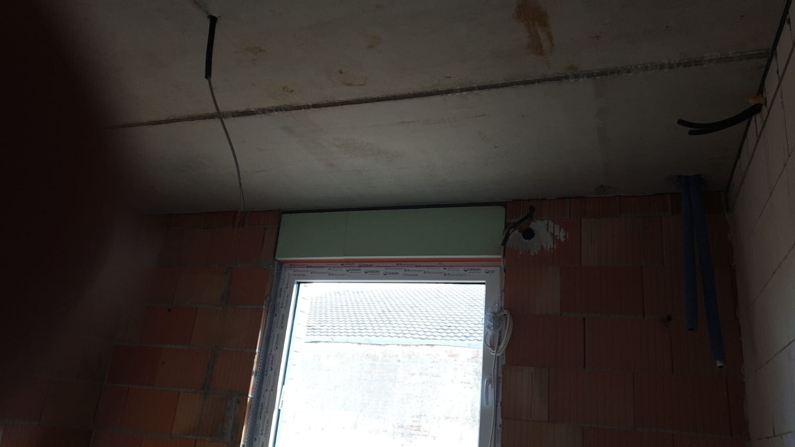 Construction site indoors: brick walls, loose cable remnants, window front with outside view, ceiling