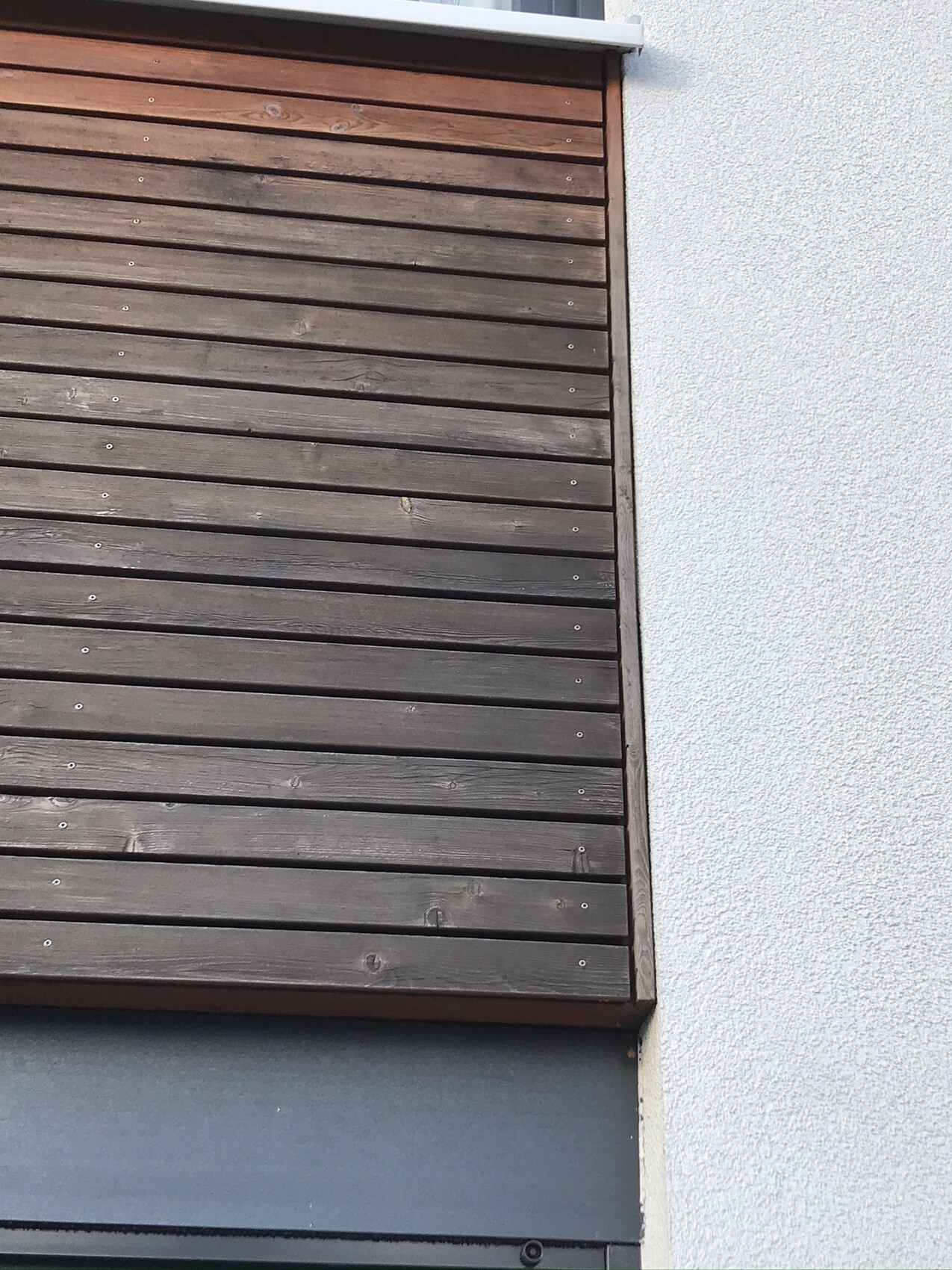 Closed horizontal wooden blinds on a light gray exterior wall.