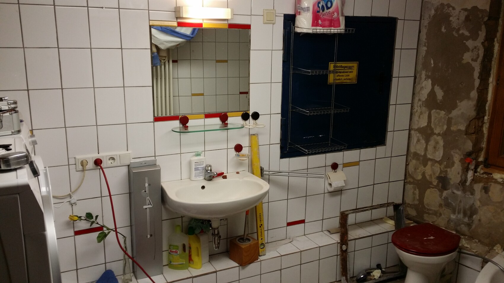 Bathroom with sink, mirror, and glass shelf; washing machine on the left, toilet on the right.