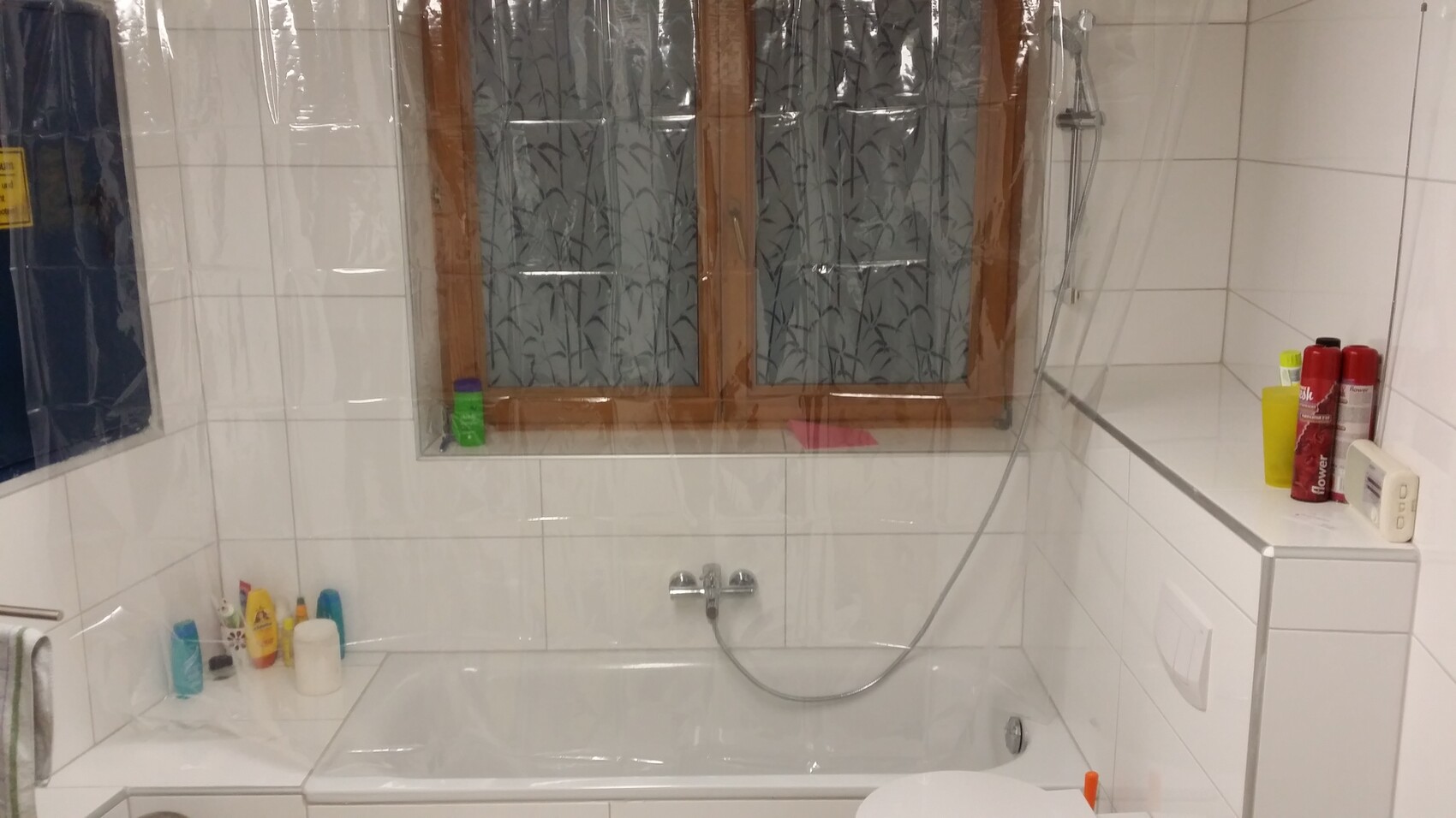Bathroom with bathtub, showerhead, window with patterned film, tiles, several shampoos on the edge.