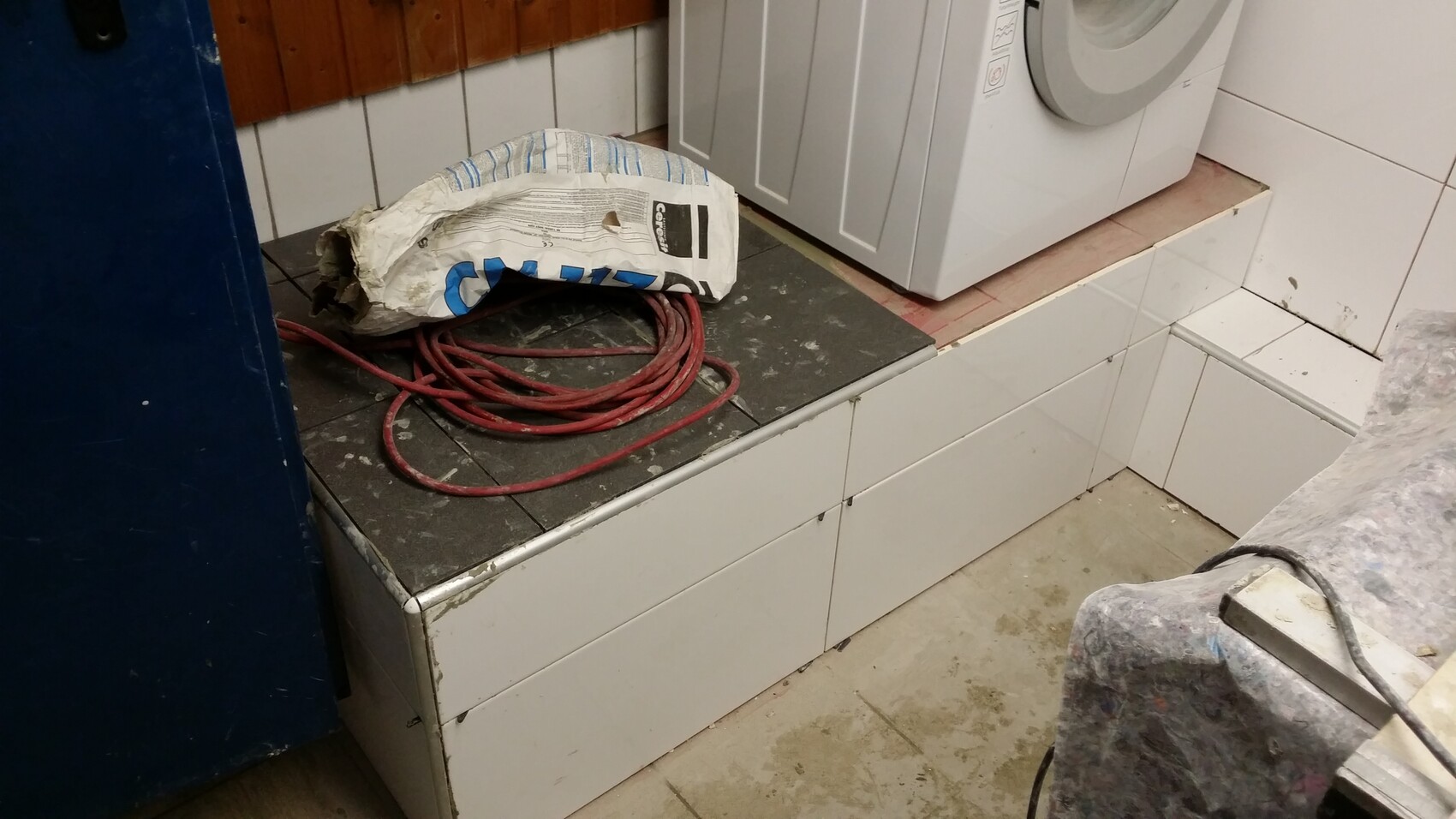 Washing machine on elevated platform, red cable mess, and cement bag in the laundry room
