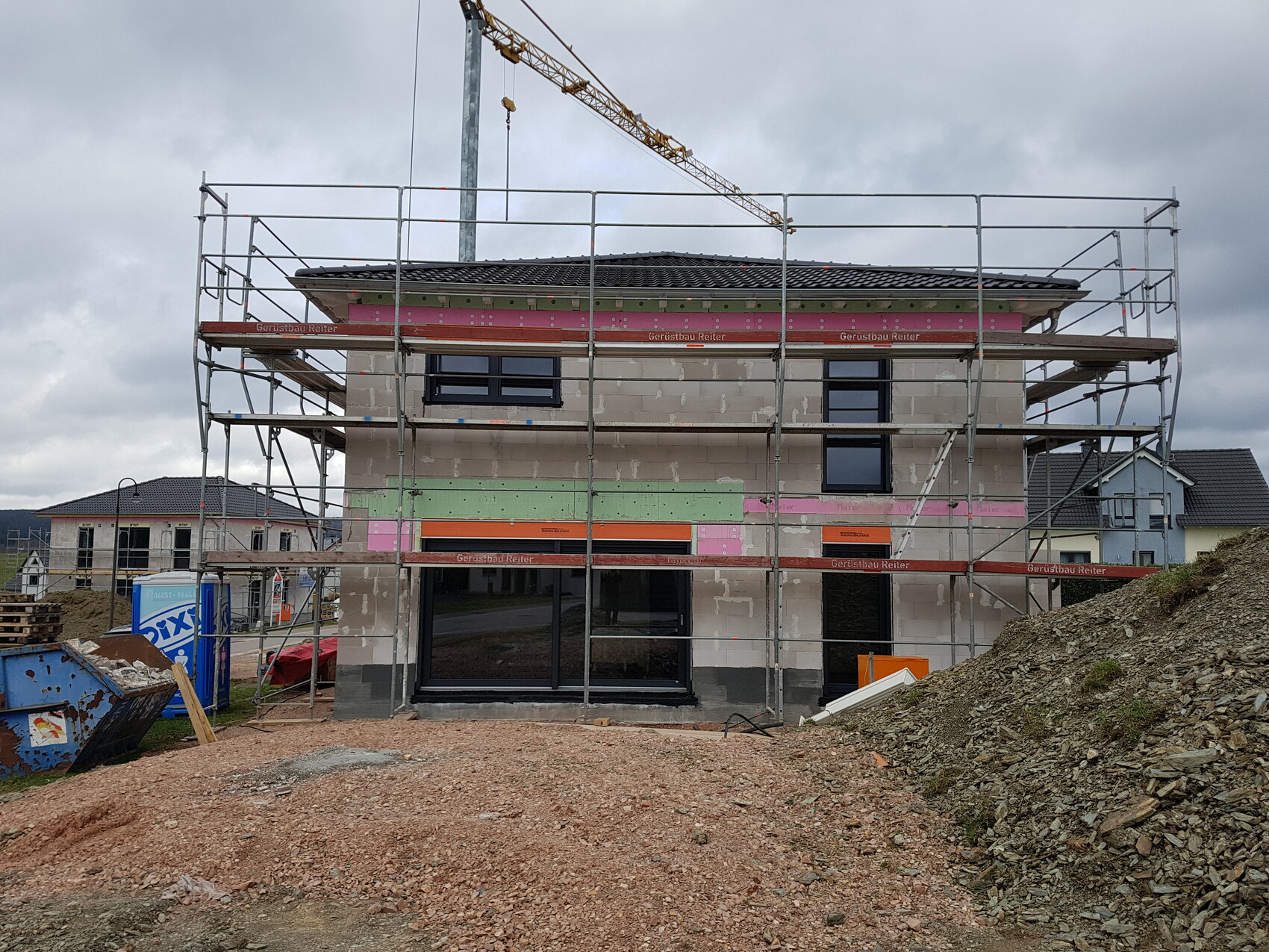 Two-story shell house, scaffolded, crane in the background, construction site.