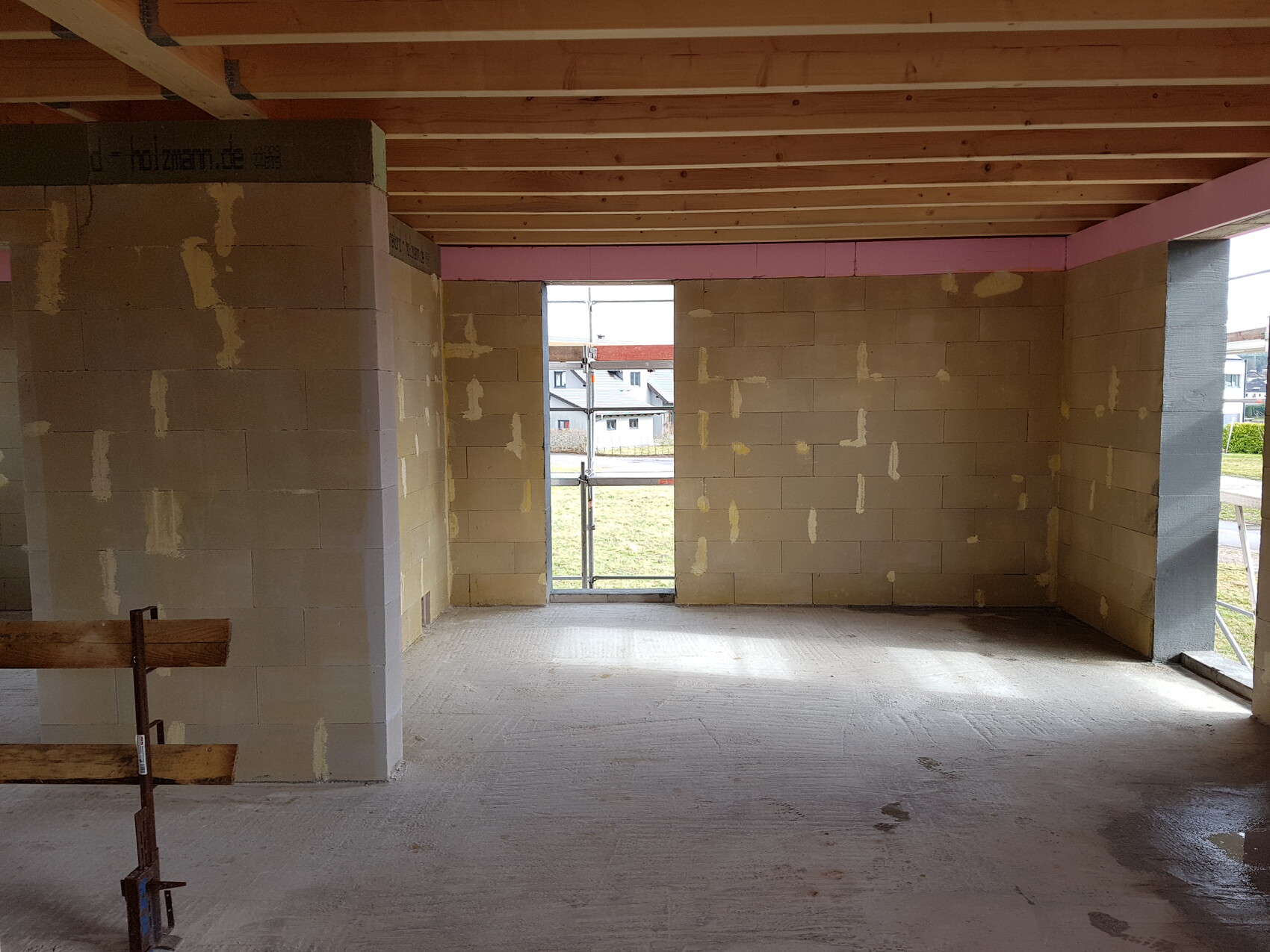Unfinished interior with concrete block walls, wooden beam ceiling, and open passage leading outside.