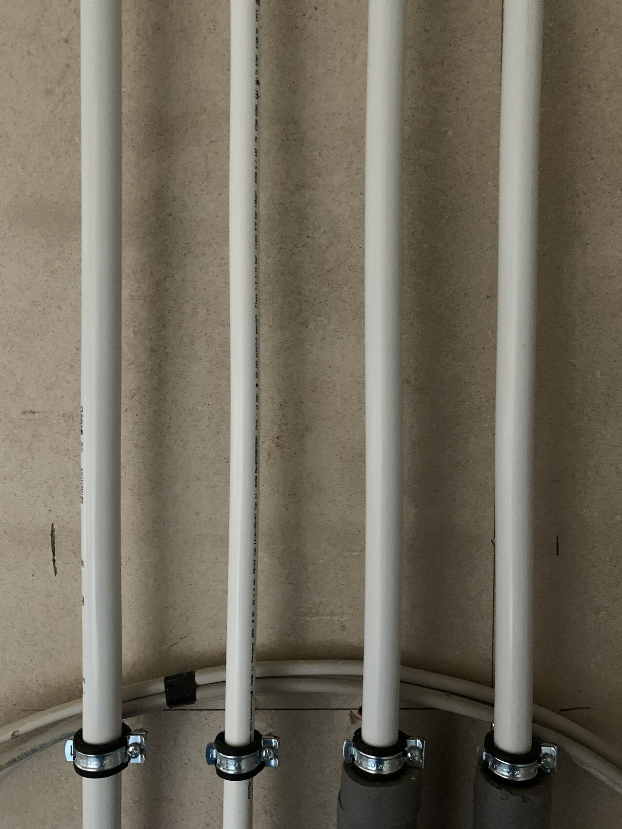 Several vertical white PVC pipes fastened to the wall with metal clamps at the bottom.