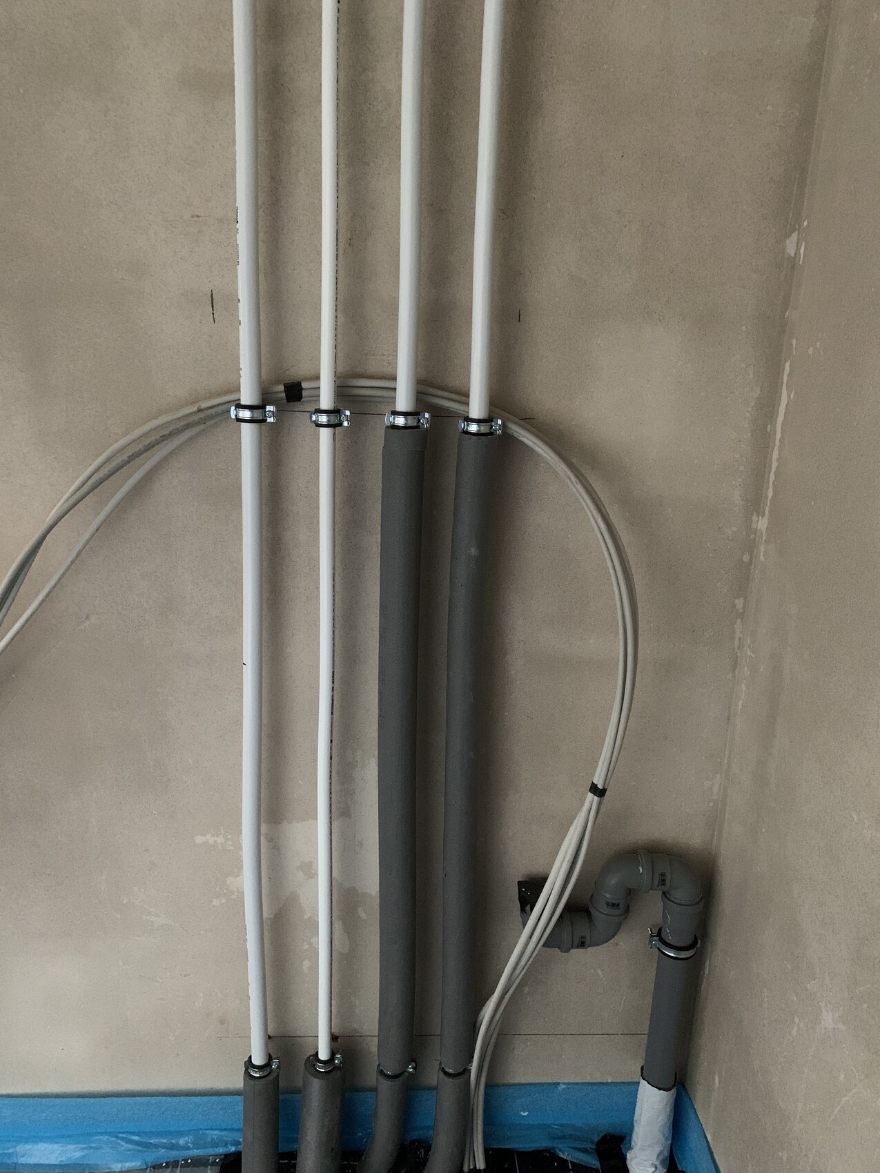 Several vertical white and gray pipes with mounting clips on a wall; hose and bend pipe visible at the bottom.