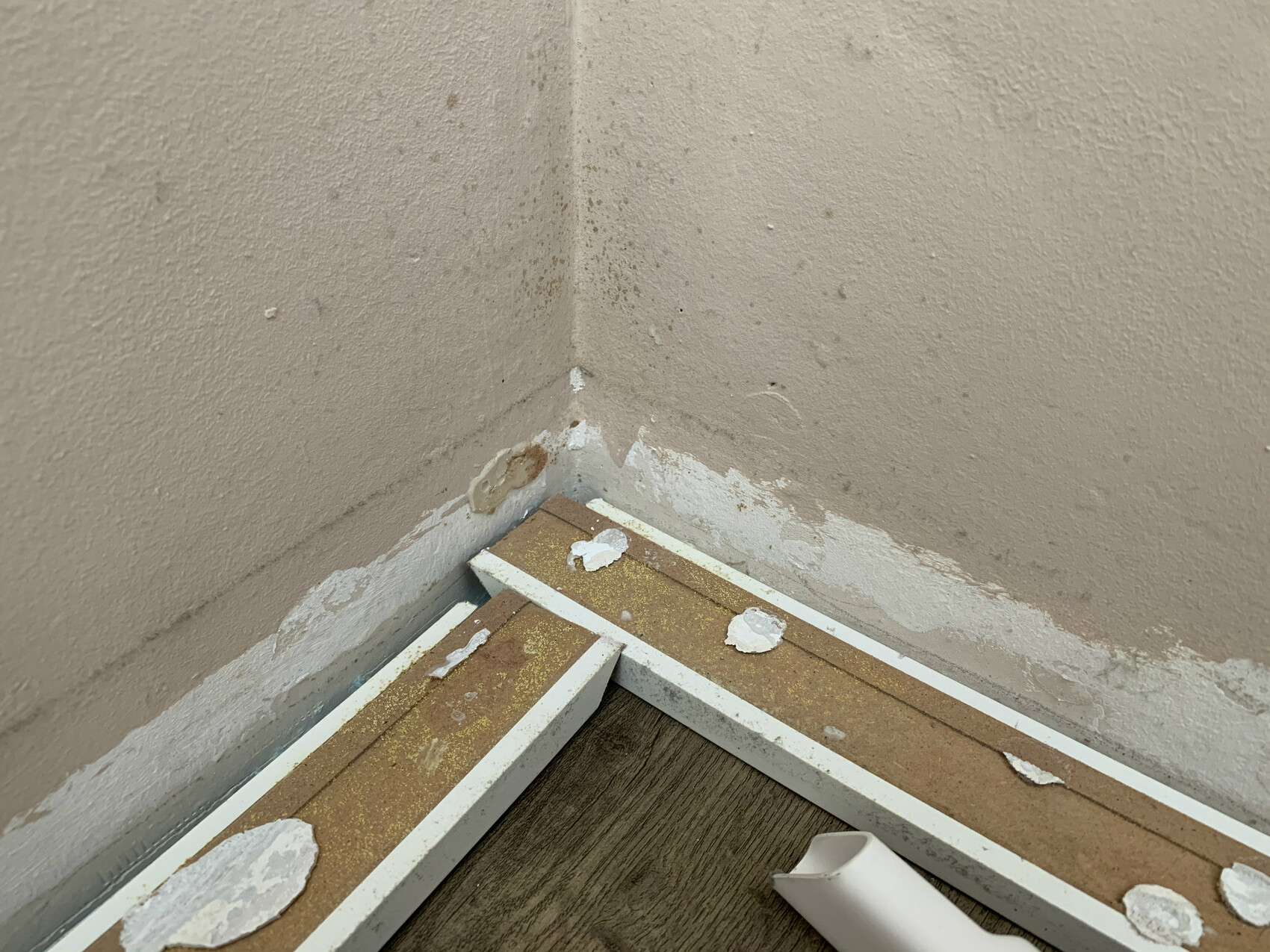 Corner of two walls with peeling paint, damaged baseboards and debris on the floor.
